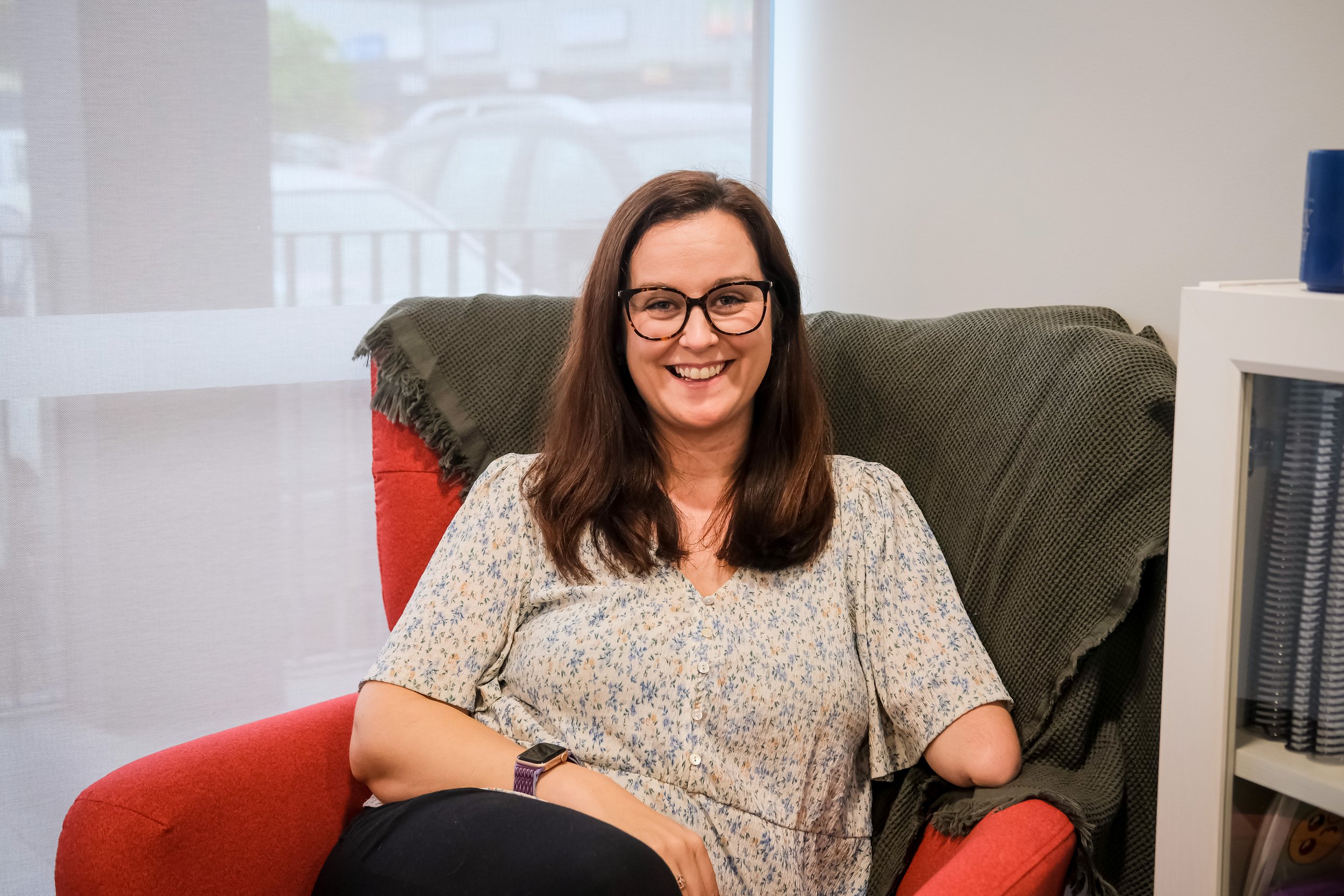 Sam - Social Work practitioner, sitting in a red chair smiling at the camera