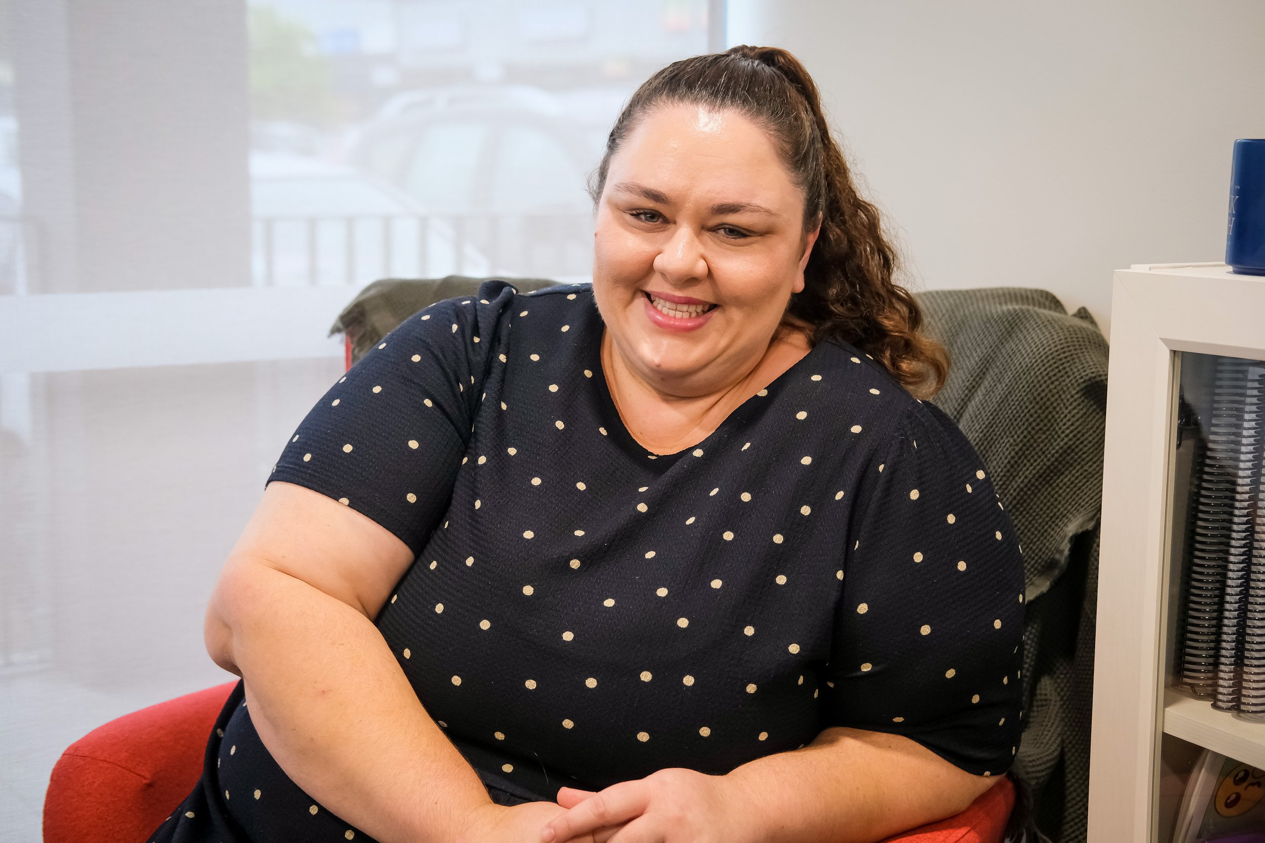 Steph - Social Work practitioner sitting in a red chair smiling at the camera